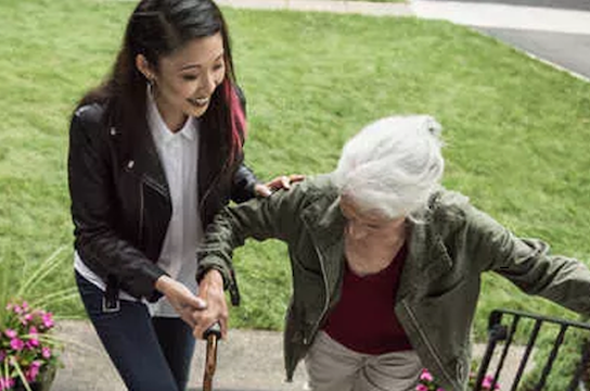Une jeune fille aide une dame âgée et munie d'une canne à monter les escaliers