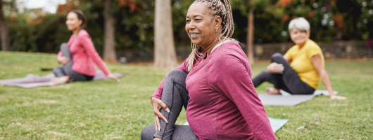 Dame faisant du yoga dans un parc. Deux autres personnes sont derrière elle. 